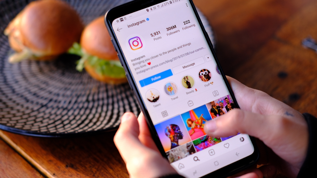 Hands holding a phone showing an Instagram profile with Story highlights.