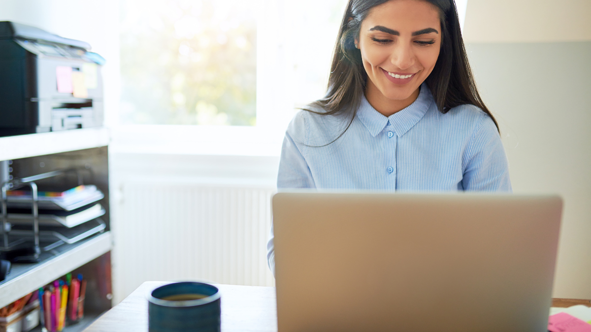 Smiling woman working at a laptop in a bright home office.