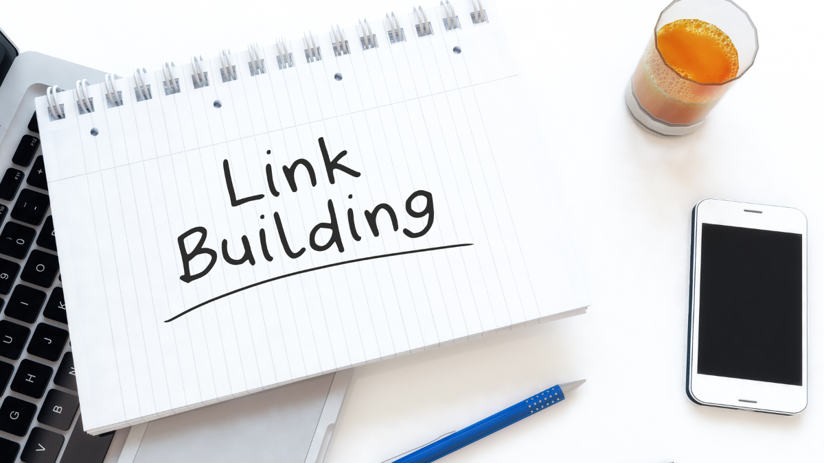 Notebook with the words 'Link Building' handwritten on it, beside a laptop, phone and pen.