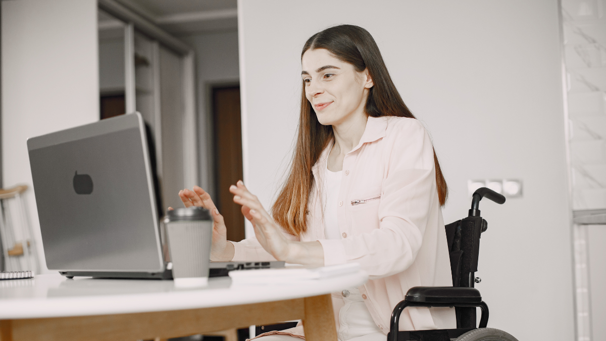Smiling woman in a wheelchair using a laptop at a table.